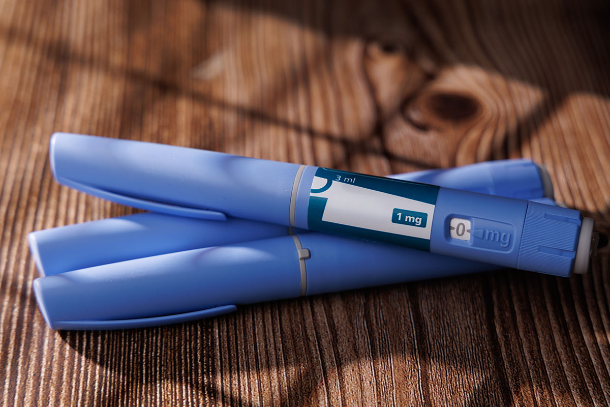 Three blue injection pens resting on a dark wooden table