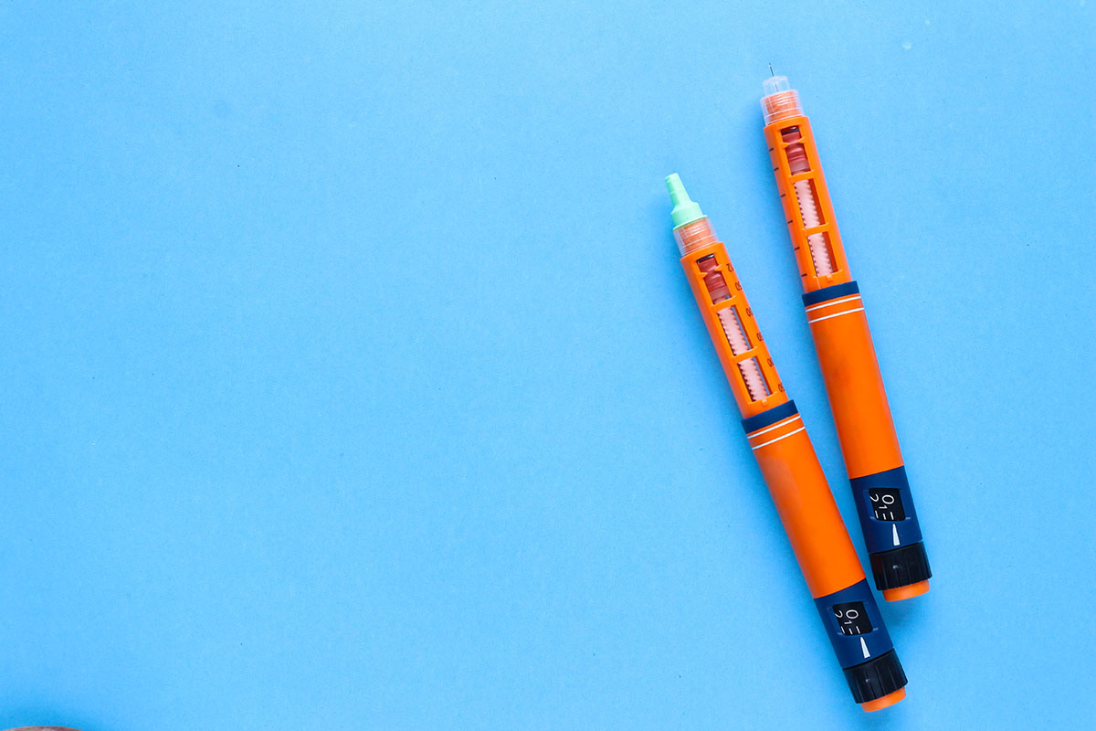 Two orange insulin injection pens lying diagonally on a plain light blue surface